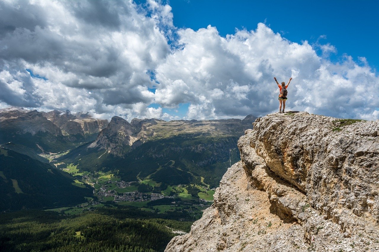 Bergkulisse im Sommer, Mensch streckt Hände an Bergkante in die Höhe